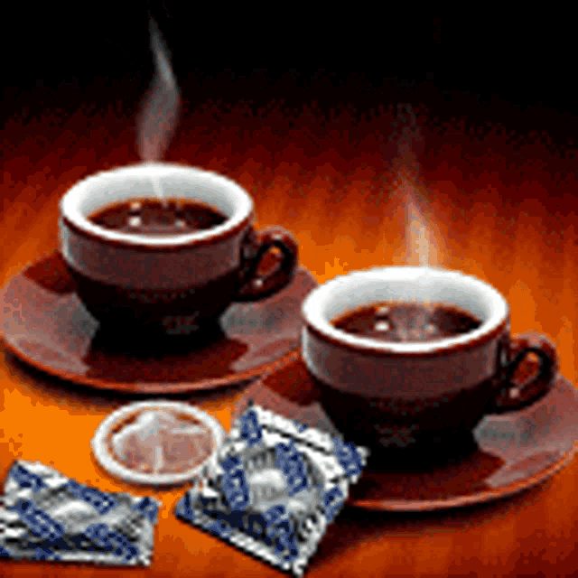 two cups of coffee on saucers next to condoms on a table