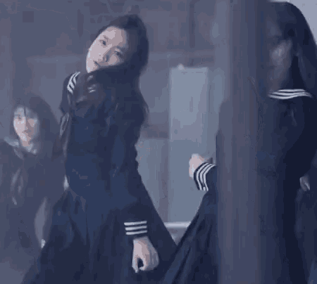 a girl in a school uniform is dancing in a dark room with other girls .