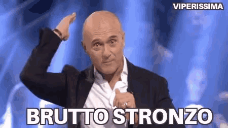 a bald man in a suit and white shirt is giving a thumbs up and says brutto stronzo