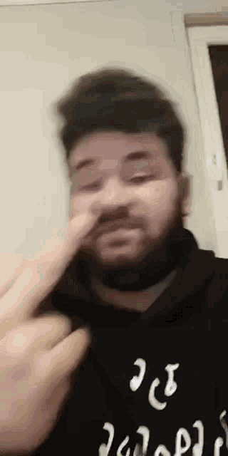 a man with a beard is blowing his nose while wearing a black shirt .