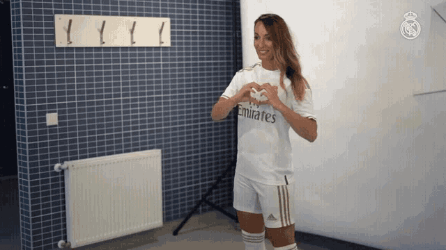a woman wearing a white emirates shirt making a heart shape with her hands