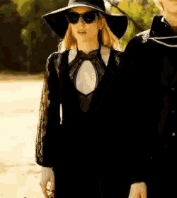 a woman wearing a hat and sunglasses is standing next to a man wearing a black jacket .