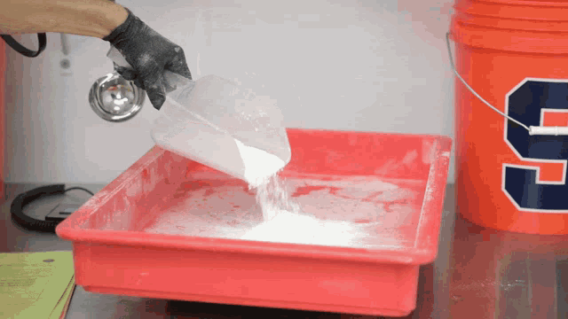 a person pouring powder into a red tray next to a bucket with the number 9 on it