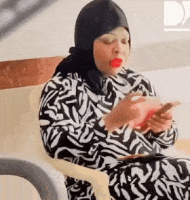 a woman wearing a hijab is sitting in a chair using a cell phone .
