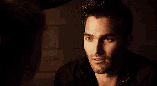 a man with a beard is looking at another man in the dark .