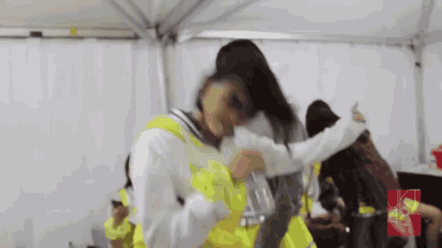 a woman in a yellow vest is hugging another woman in a white shirt in a tent .