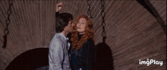 a man and woman kissing in front of a brick wall with imgplay at the bottom of the screen