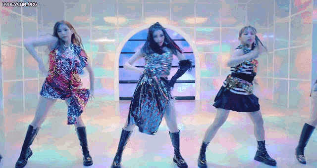 a group of three women are dancing in a room with a colorful background .