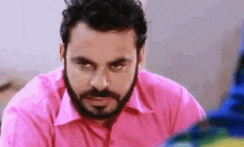 a man with a beard and a pink shirt is looking at the camera .