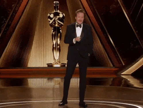 a man in a tuxedo is standing in front of a statue