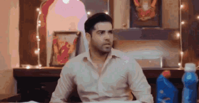 a man in a white shirt is sitting at a table in a room with a bottle of detergent in front of him .