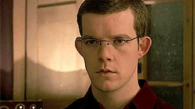 a young man wearing glasses is looking at the camera .