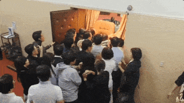a large group of people are gathered in a room and one of them has a timex shirt on