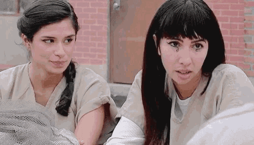 two women are sitting next to each other in a jail cell .
