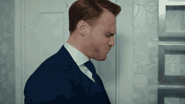 a man in a suit and tie is standing in front of a door and looking down .