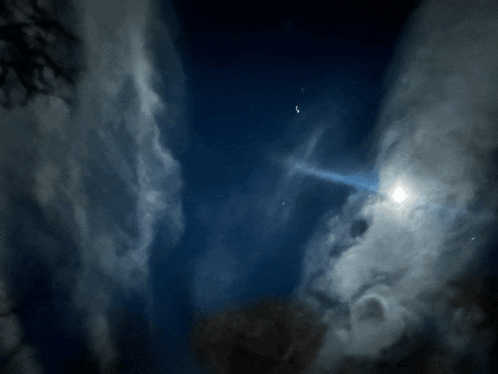 a bright light shines through the clouds in a dark night sky