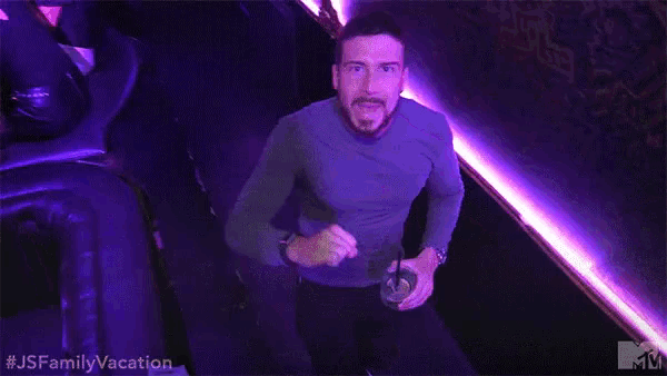 a man in a purple shirt is holding a drink in a club .