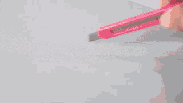 a person is holding a pink knife in their hand and cutting a piece of paper .