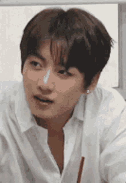 a close up of a young man wearing a white shirt with a straw in his mouth .