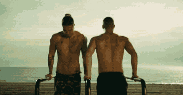 two men are doing push ups on a beach