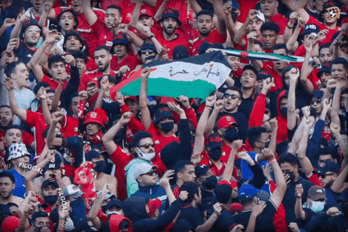 a crowd of people in a stadium holding up a flag with arabic writing on it