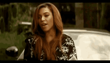 a woman with long hair is standing next to a car and talking to someone .