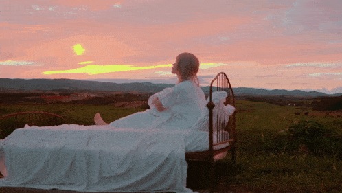 a woman laying on a bed in a field looking at the sunset