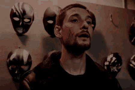 a man with a beard stands in front of a wall of masks