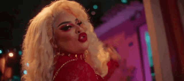 a drag queen with blonde hair and red lips is wearing a red top