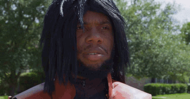 a man with dreadlocks and a beard is wearing a red vest