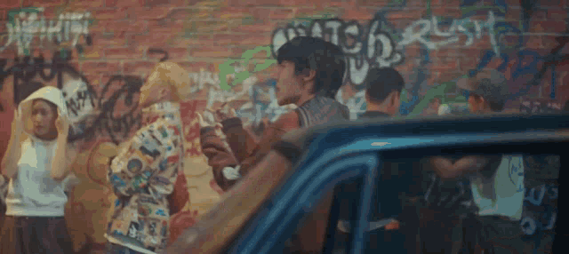 a group of young people are standing in front of a brick wall with graffiti on it .