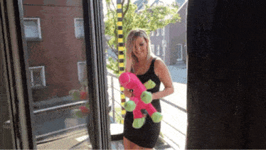 a woman in a black dress is holding a stuffed animal on a balcony