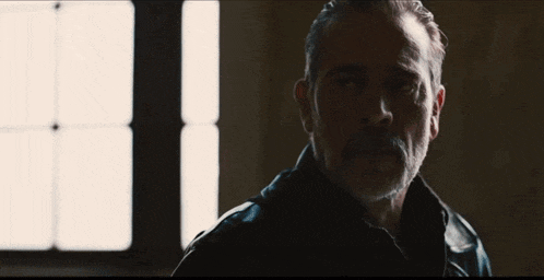 a man with a beard wearing a black leather jacket stands in front of a window