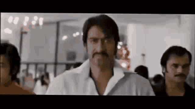 a man with a mustache is standing in front of a crowd of people .