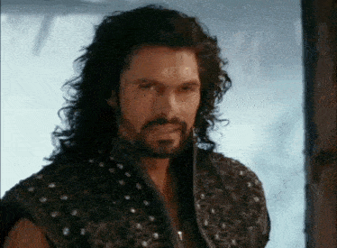 a man with long hair and a beard wearing a studded vest .