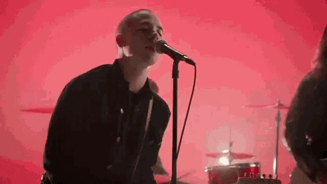 a man is singing into a microphone while playing a guitar on a red background .