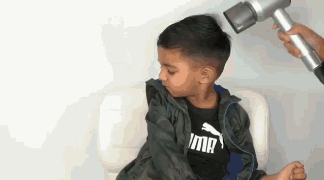 a young boy is sitting on a chair while a person blow dry his hair .