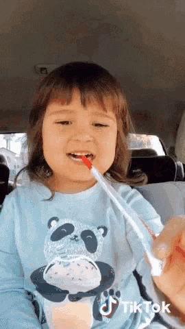 a little girl in a panda shirt is brushing her teeth with a red toothbrush ..