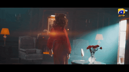 a woman in a red robe is standing in a room with a vase of flowers on a table