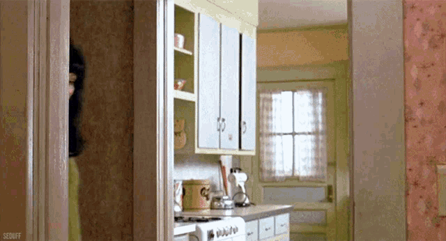 a woman is standing in a kitchen with a stove and a coffee pot on the counter .