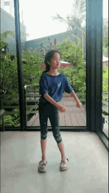 a little girl is dancing in front of a window .