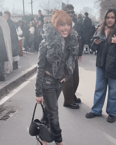 a woman with red hair and a black jacket is holding a black purse