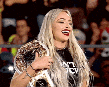 a woman in a black shirt that says n't touch is holding a wrestling championship belt