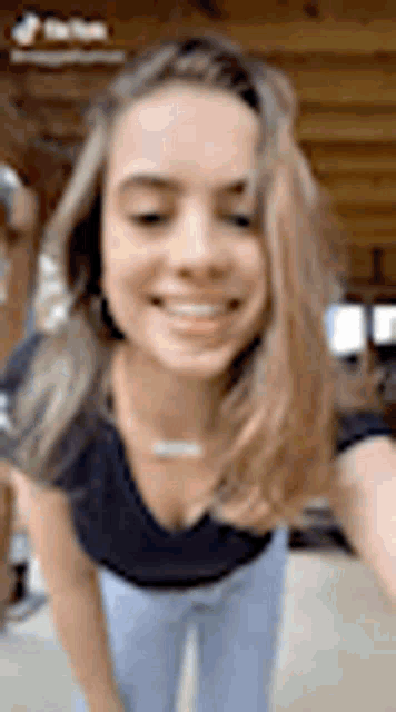 a woman in a black shirt and blue jeans is taking a selfie and smiling .