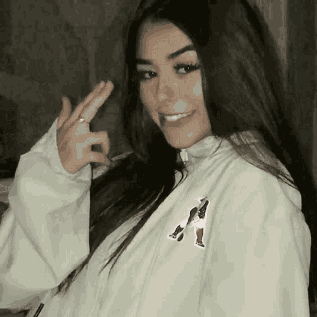 a woman wearing a white jacket with the letter a on it giving the middle finger