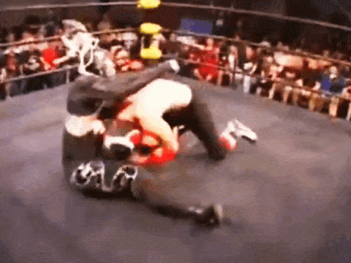 two men are wrestling in a ring with a crowd in the background .