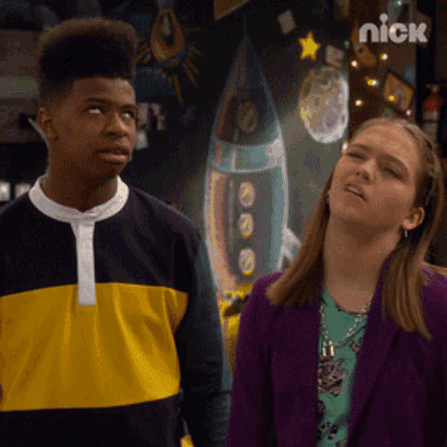 a boy and a girl are standing in front of a wall with a picture of a rocket on it