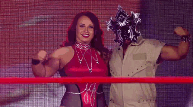 a woman in a red top flexes her muscles next to a man wearing a mask