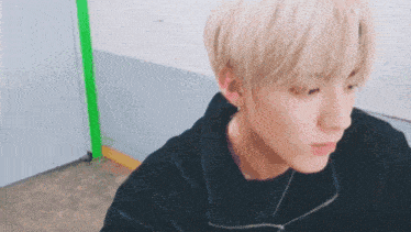 a young man with blonde hair is wearing a black jacket and a black sweater .