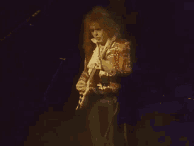 a man in a red jacket is playing a guitar on a stage